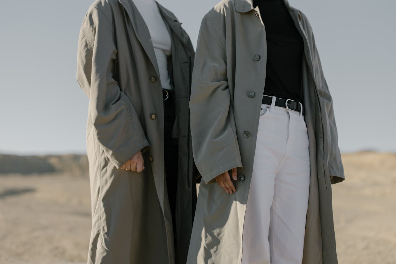 who-we-are Two fashionable women wearing trench coats in a desert landscape, exuding minimalist style.